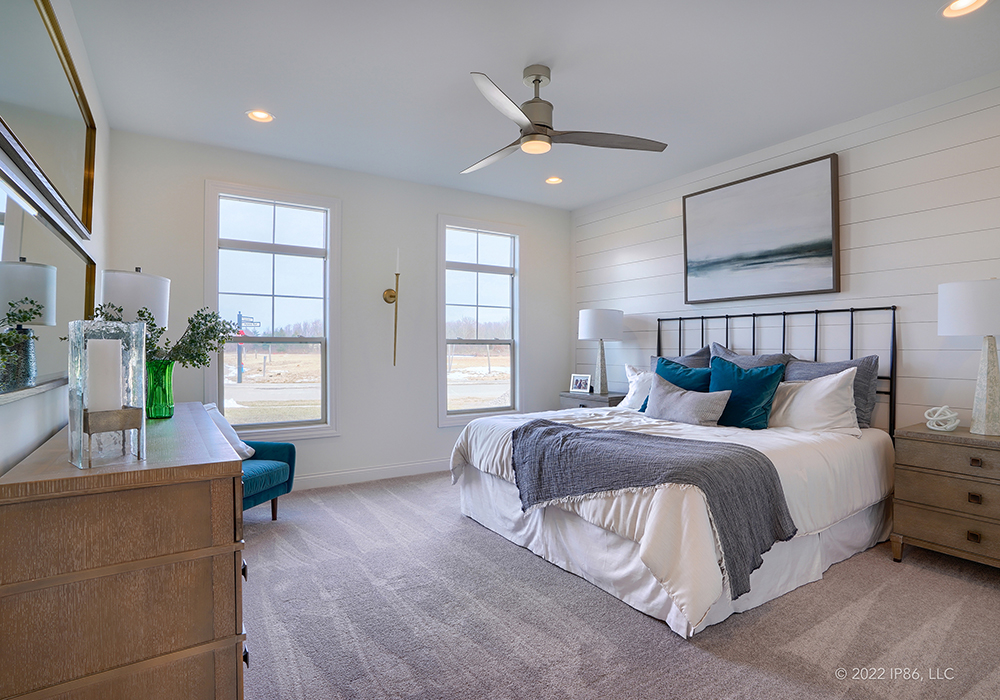 A stylish bedroom featuring a bed, dresser, and ceiling fan, designed as the Provenance model by New Leaf Homes.