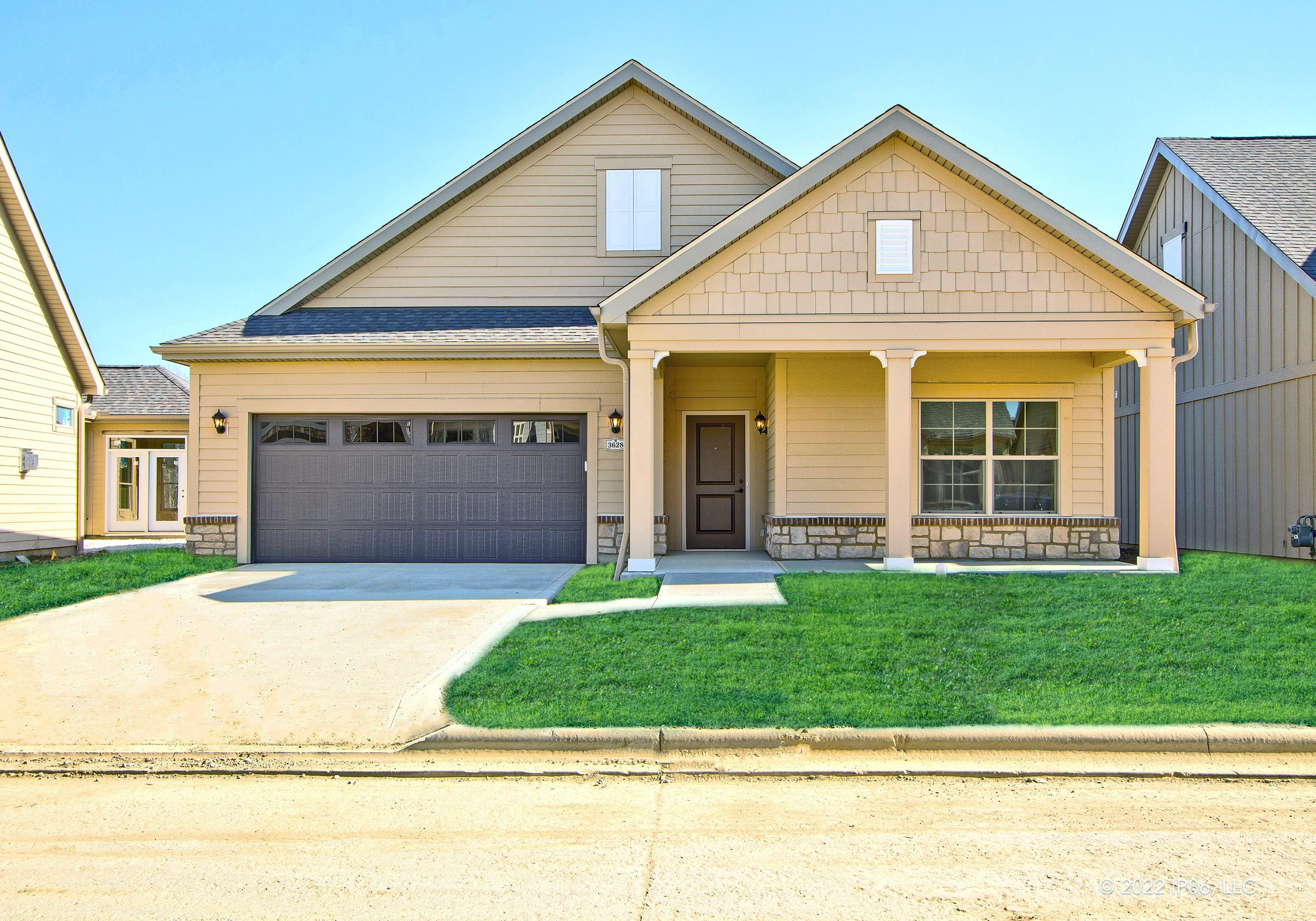 Exterior view of the Capri model home by New Leaf Homes with beige siding, a two-car garage, and a welcoming front porch.