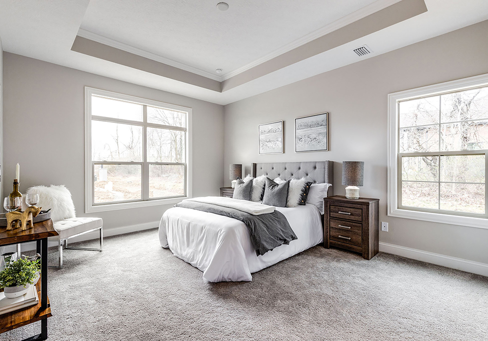 Spacious modern bedroom with tray ceiling, large windows, and neutral decor in the Palazzo model home by New Leaf Homes.