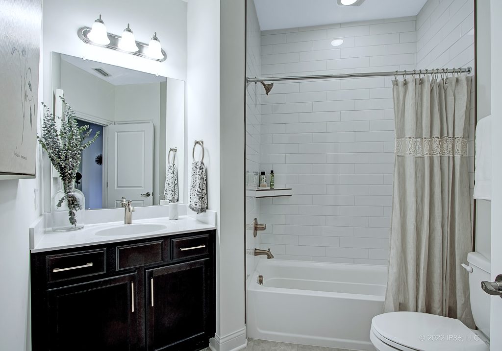A modern bathroom featuring a shower, toilet, and sink, designed as the Promenade model by New Leaf Homes.