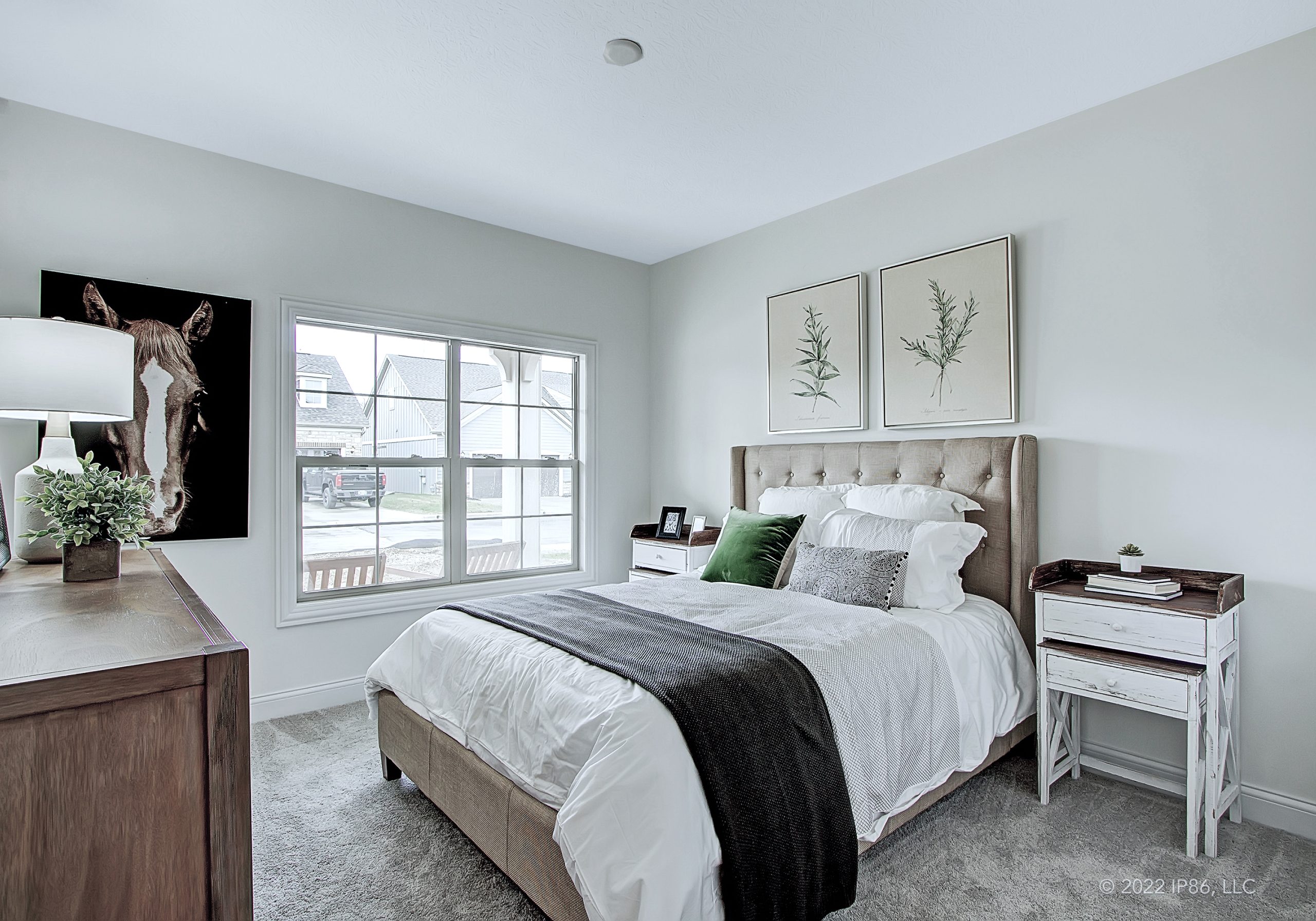 A stylish bedroom featuring a bed, dresser, and window, showcasing the Promenade model by New Leaf Homes.