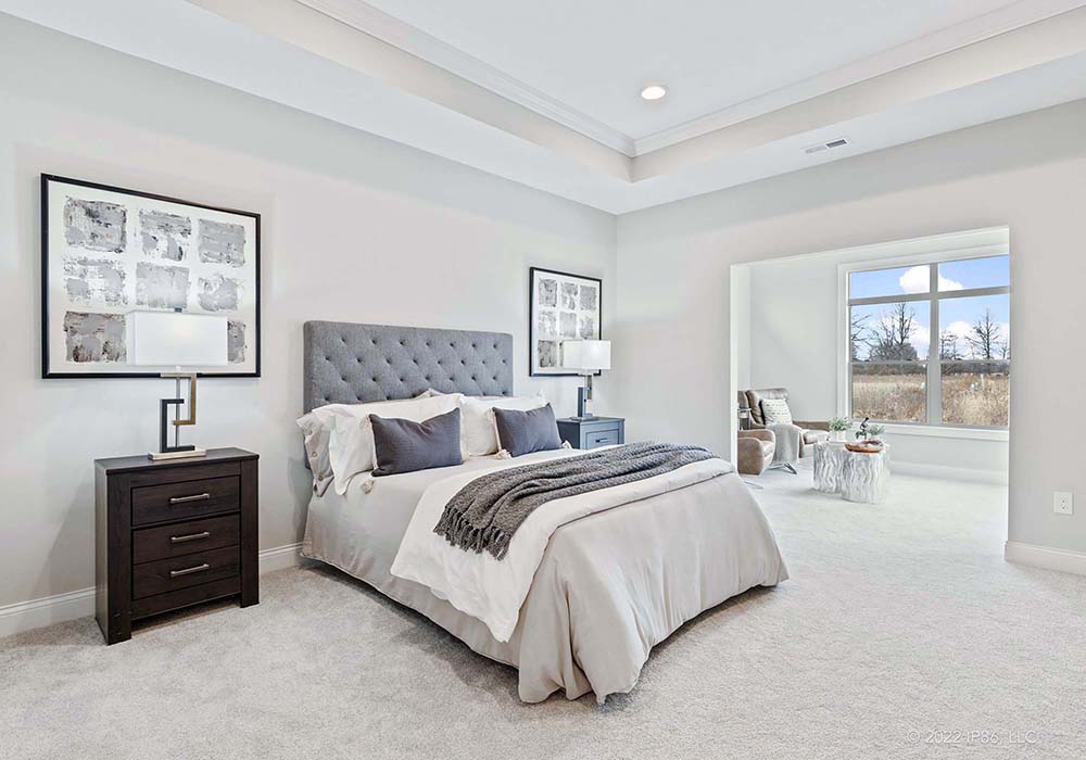 A spacious master bedroom featuring a gray bed and carpet, designed as the Torino model by New Leaf Homes.