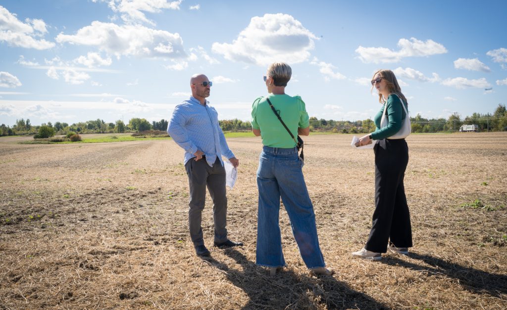 Three individuals converse in a field as they assess the land for a new development project.