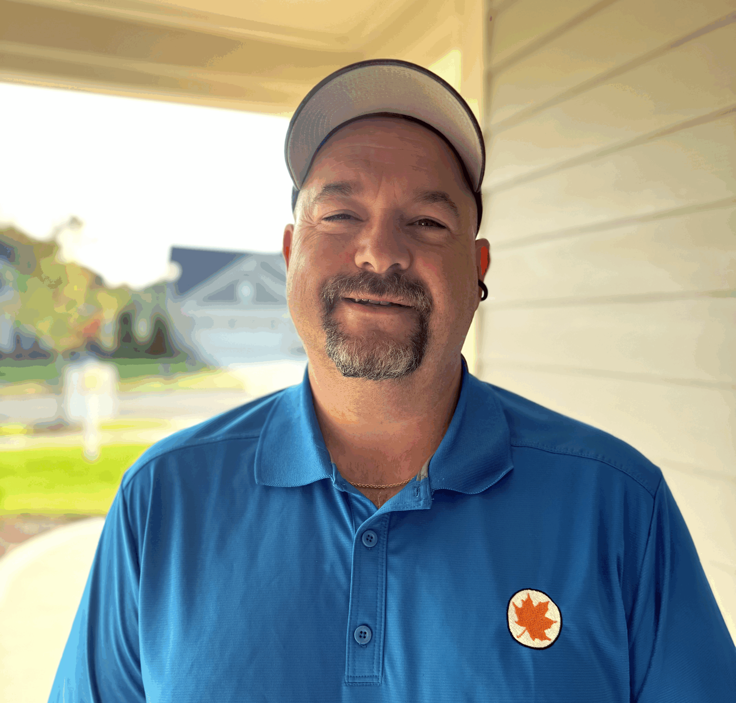 Headshot of Mike Kundrat, Assistant Project Manager at New Leaf Homes, wearing a blue New Leaf polo shirt and a white cap, smiling outdoors.